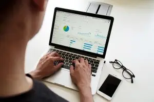 Eine Frau blickt auf Diagramme auf ihrem Notebook-Bildschirm. Vor ihr liegen eine Brille und ein Smartphone.