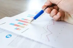 Papier mit Diagrammen liegt auf einem Tisch. Ein Mann fährt mit dem Kugelschreiber darüber.