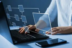 Workflow Ein Mann blickt auf sein Notebook. Über der Tastatur sind Kästchen mit Pfeilen verbunden und verdeutlichen den digitalen Überblick über sämtliche Prozesse.