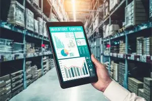 AdobeStock_468707974_EBC Ein Mann hält ein Tablet in einem Hochregallager in der Hand und hat so seinen Lagerbestand im Blick.