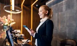 Sehr freundlich lächelnde Mitarbeiterin mit Tablet an der Hotel-Rezeption