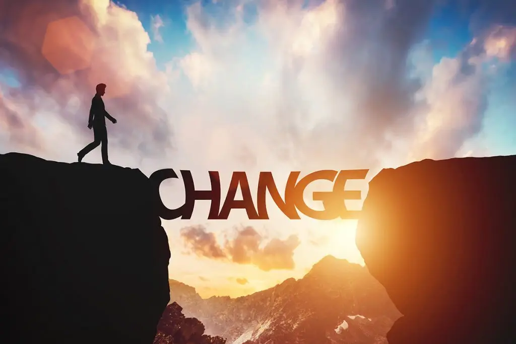Mann steht vor einer Schlucht mit dem Wort "Change" als Brücke vor einem Sonnenaufgang in den Bergen