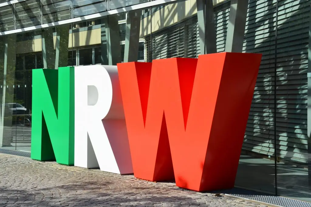 Die Buchstaben NRW stehen groß in Landesfarben vor einem Gebäude